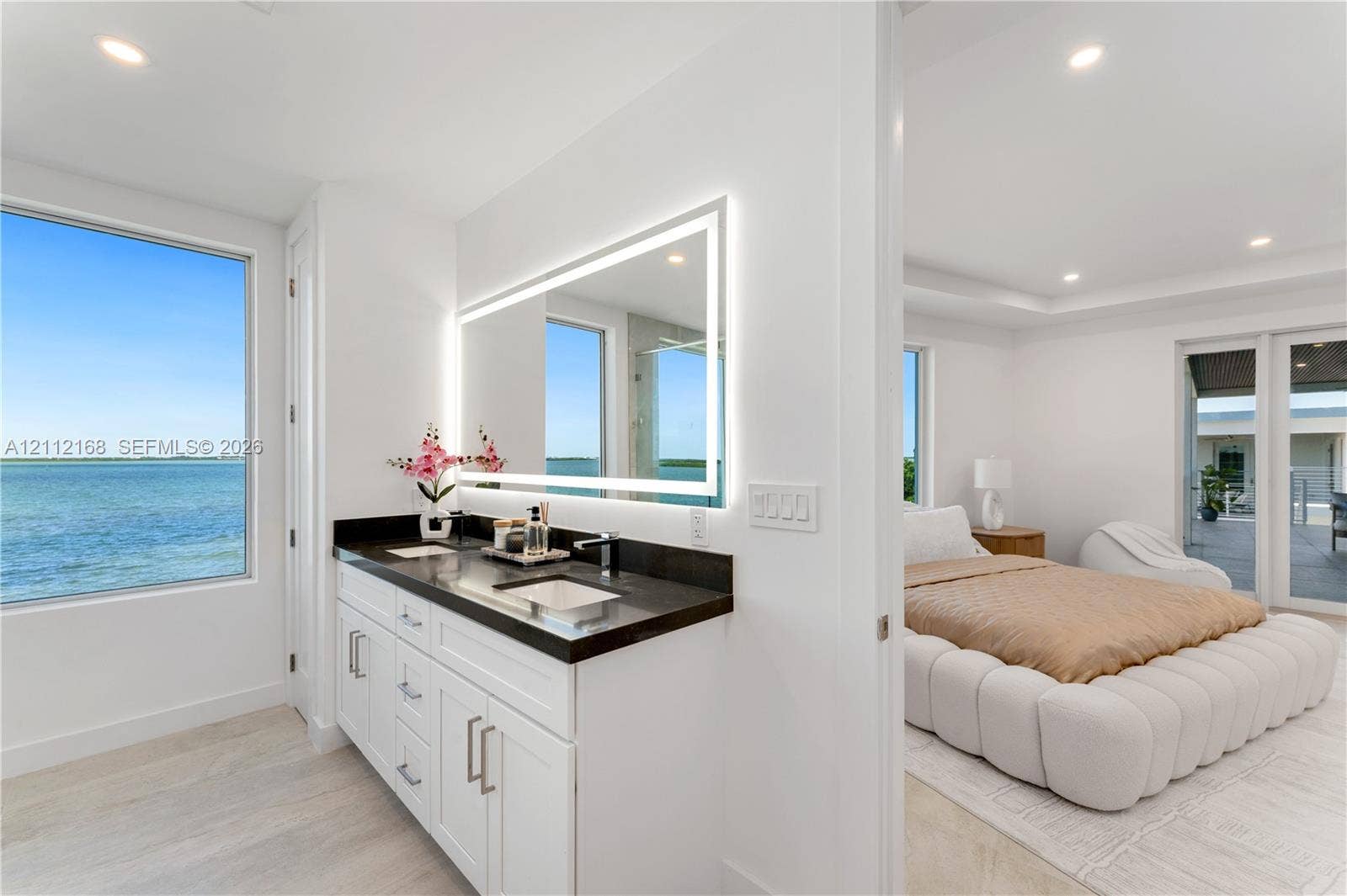 1041 E Buttonwood Drive, Sugarloaf Key, FL 33042 Bathroom vanity featuring white cabinetry, a dark countertop, integrated dual sinks, and an illuminated rectangular mirror, complemented by water-front exterior exposure