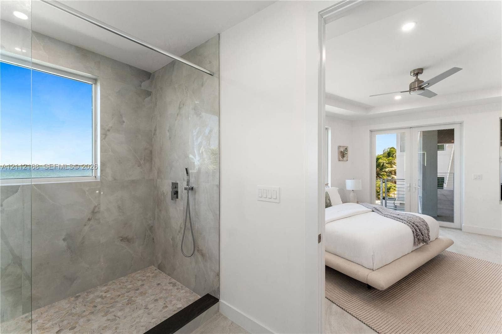1041 E Buttonwood Drive, Sugarloaf Key, FL 33042 Walk-in shower featuring large-format tile surround, integrated window, handheld showerhead, pebble-finish flooring, and a frameless glass partition