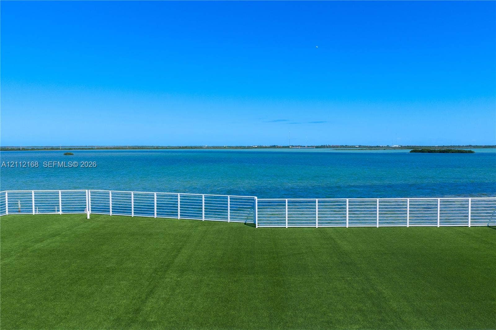 1041 E Buttonwood Drive, Sugarloaf Key, FL 33042 Outdoor space featuring synthetic turf and a white horizontal-slat metal railing, set against a waterfront backdrop