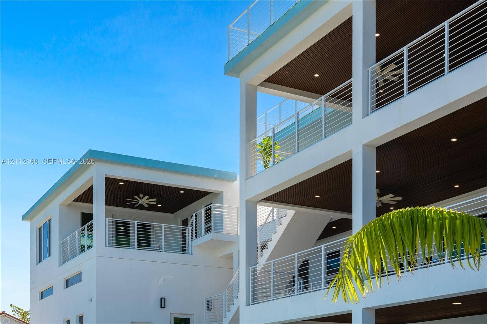 1041 E Buttonwood Drive, Sugarloaf Key, FL 33042 Multi-level exterior featuring stacked covered balconies, white horizontal railings, recessed lighting, and dark-toned plank ceilings