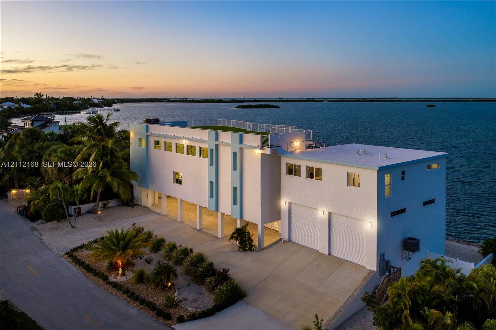 1041 E Buttonwood Drive, Sugarloaf Key, FL 33042 Waterfront residence featuring a rooftop terrace, multi-level exterior structure, two-car garage, concrete driveway, and pilings foundation