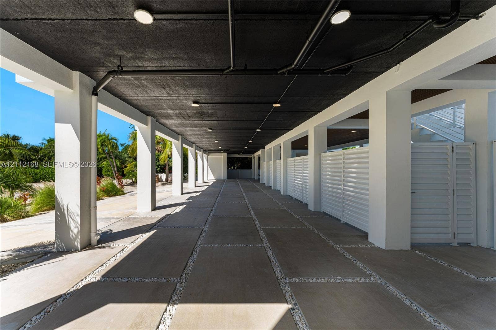 1041 E Buttonwood Drive, Sugarloaf Key, FL 33042 Covered ground-level parking area featuring concrete pavers, white louvered privacy screens, recessed lighting, and exposed ceiling structure