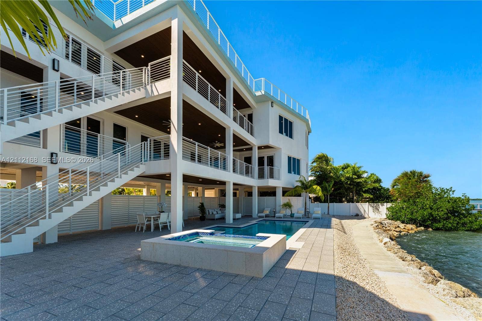 1041 E Buttonwood Drive, Sugarloaf Key, FL 33042 Multi-level residence featuring tiered outdoor balconies with horizontal railings, stone-tiled patio, in-ground swimming pool, and integrated spa