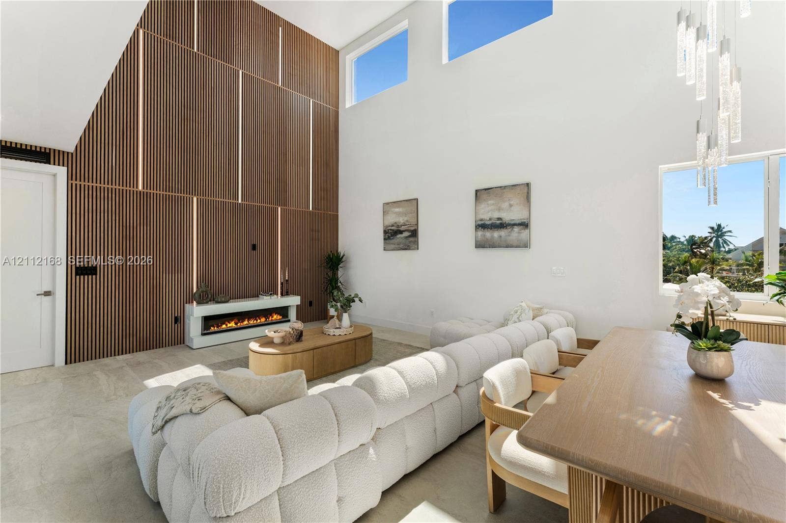 1041 E Buttonwood Drive, Sugarloaf Key, FL 33042 Double-height ceilings with clerestory windows, vertical slat wood-finish accent wall with integrated lighting, built-in linear electric fireplace, stone-finish flooring, and multi-light hanging chandelier