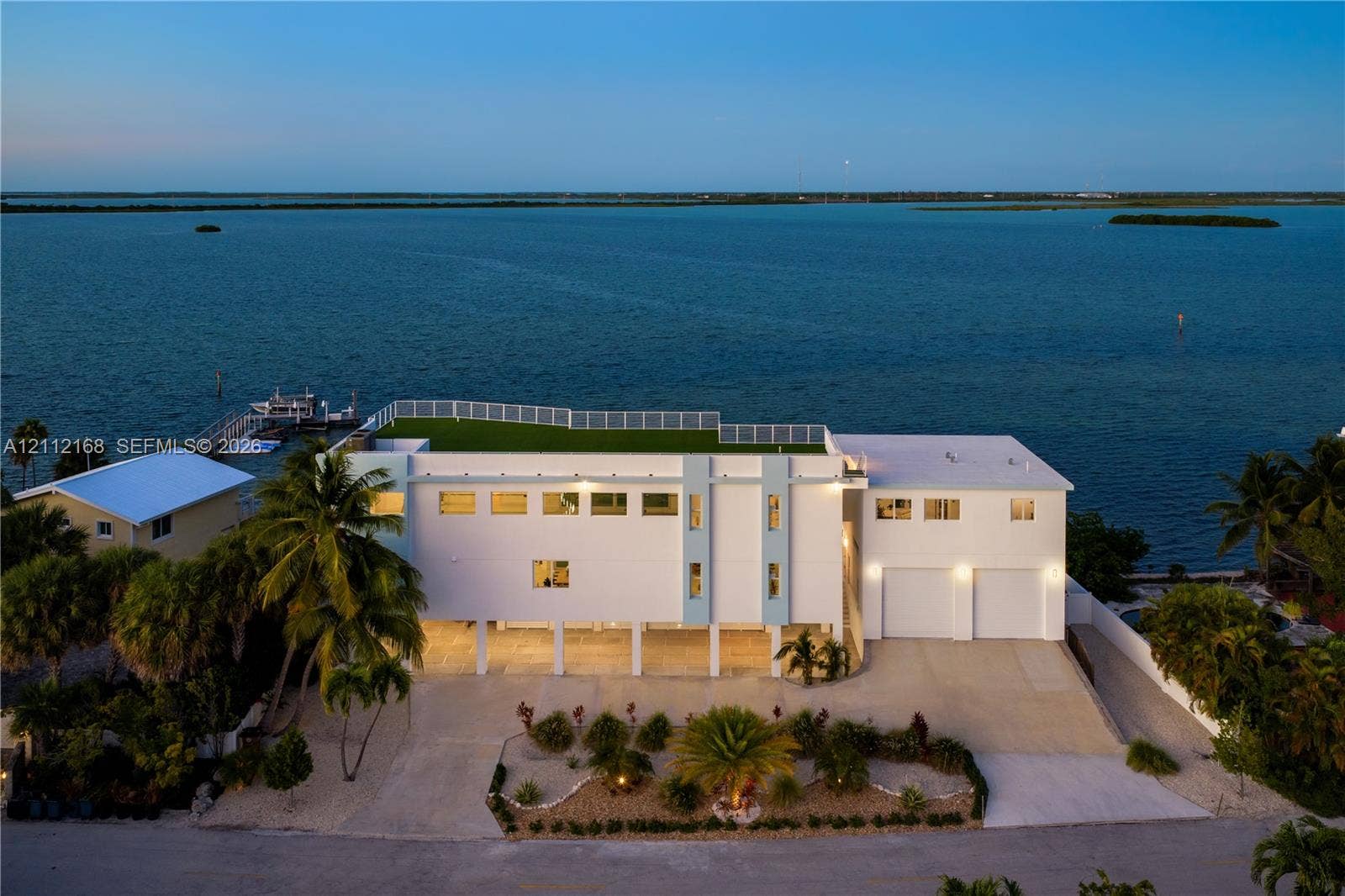 1041 E Buttonwood Drive, Sugarloaf Key, FL 33042 Waterfront estate featuring a rooftop terrace, elevated structural design, integrated two-car garage, private dock, and mature palm landscaping