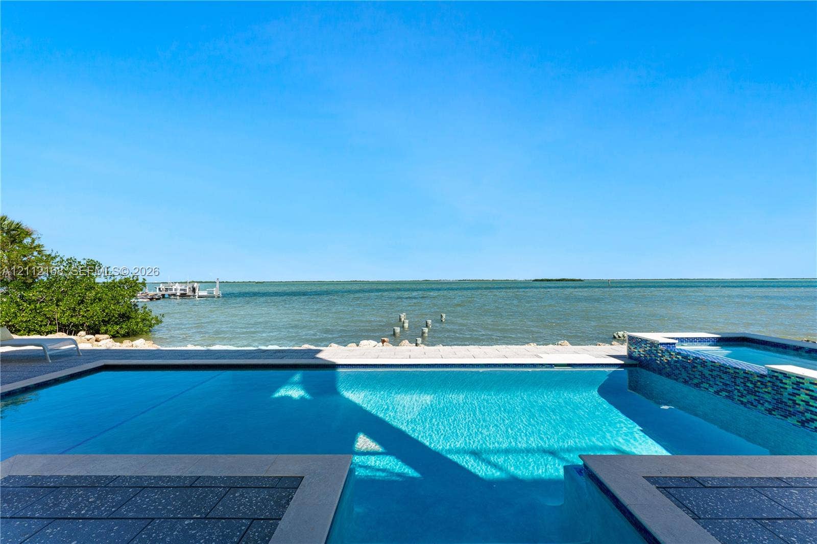 1041 E Buttonwood Drive, Sugarloaf Key, FL 33042 In-ground swimming pool featuring a tiled spillover spa, stone paver decking, and direct water frontage