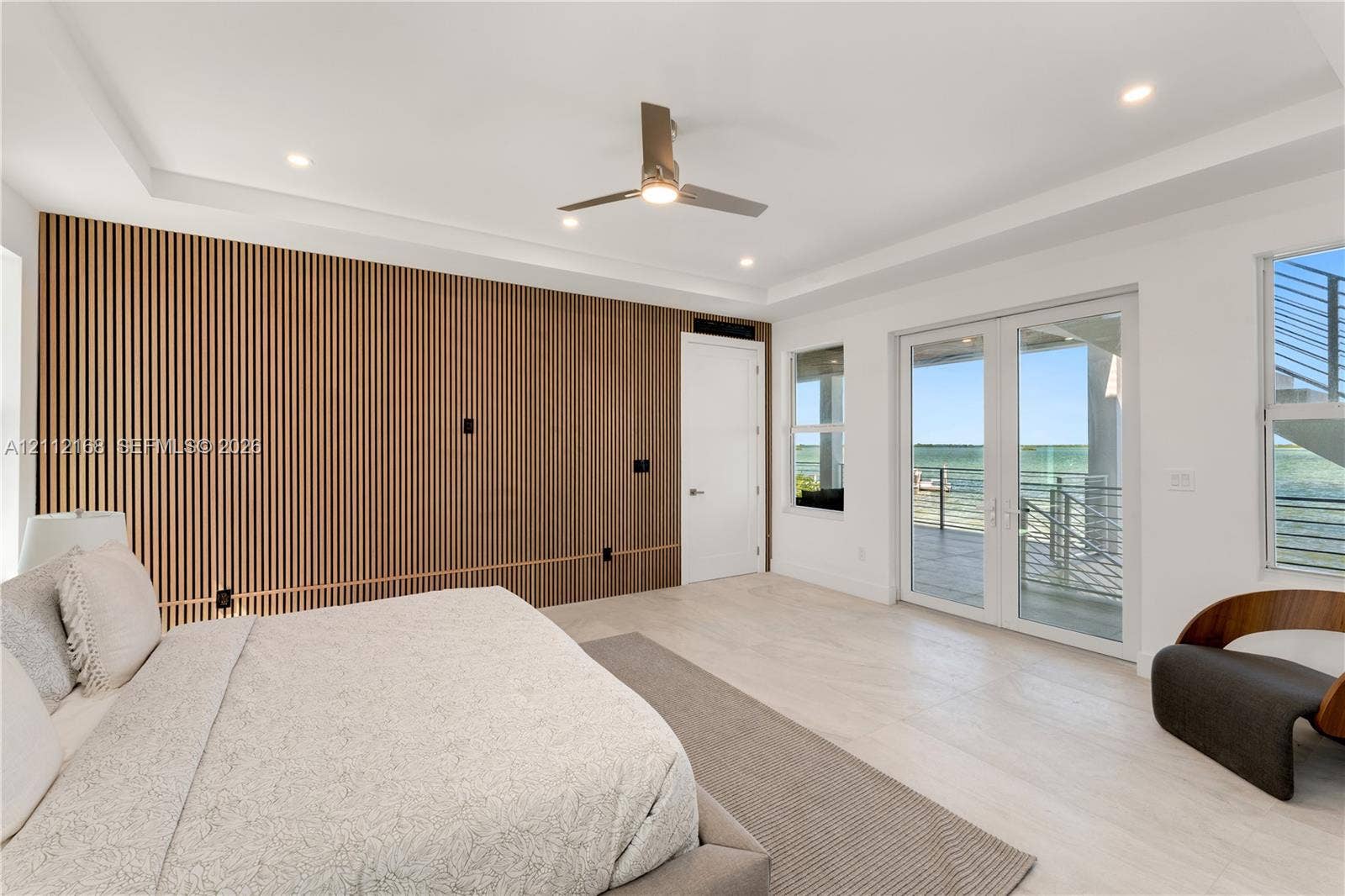 1041 E Buttonwood Drive, Sugarloaf Key, FL 33042 Slatted wood-finish accent wall, tray ceiling with recessed lighting, light-toned wood-finish flooring, and glass French doors leading to an exterior balcony