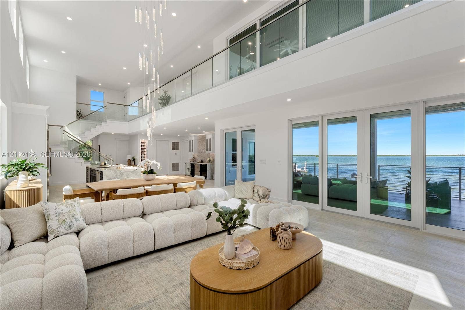 1041 E Buttonwood Drive, Sugarloaf Key, FL 33042 Expansive open-concept living area featuring double-height ceilings, a floor-to-ceiling glass-paneled mezzanine, multi-panel sliding glass doors, and a linear pendant light fixture