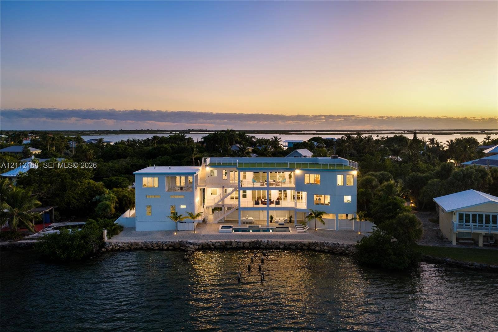 1041 E Buttonwood Drive, Sugarloaf Key, FL 33042 Waterfront residence featuring multi-level balconies, an in-ground swimming pool, a rock-lined shoreline, and a rooftop terrace