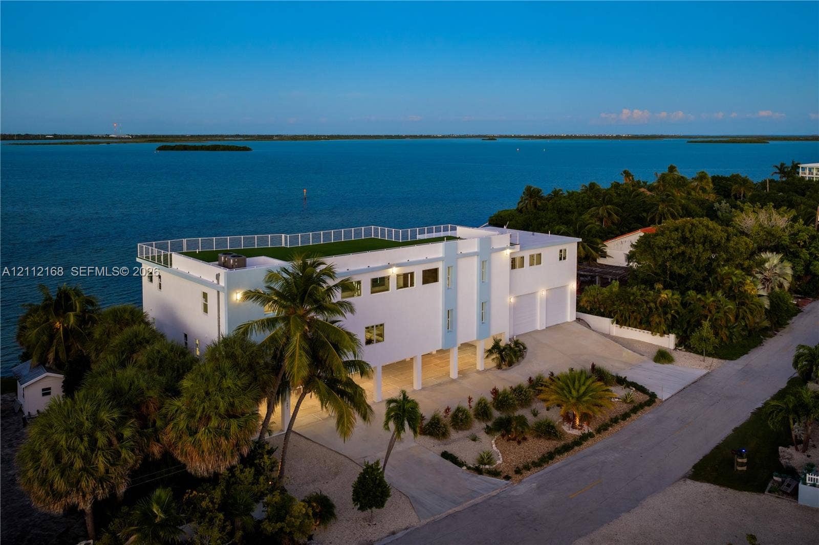 1041 E Buttonwood Drive, Sugarloaf Key, FL 33042 Multi-story waterfront residence featuring a rooftop terrace, elevated construction, multi-car garage, and established landscaping