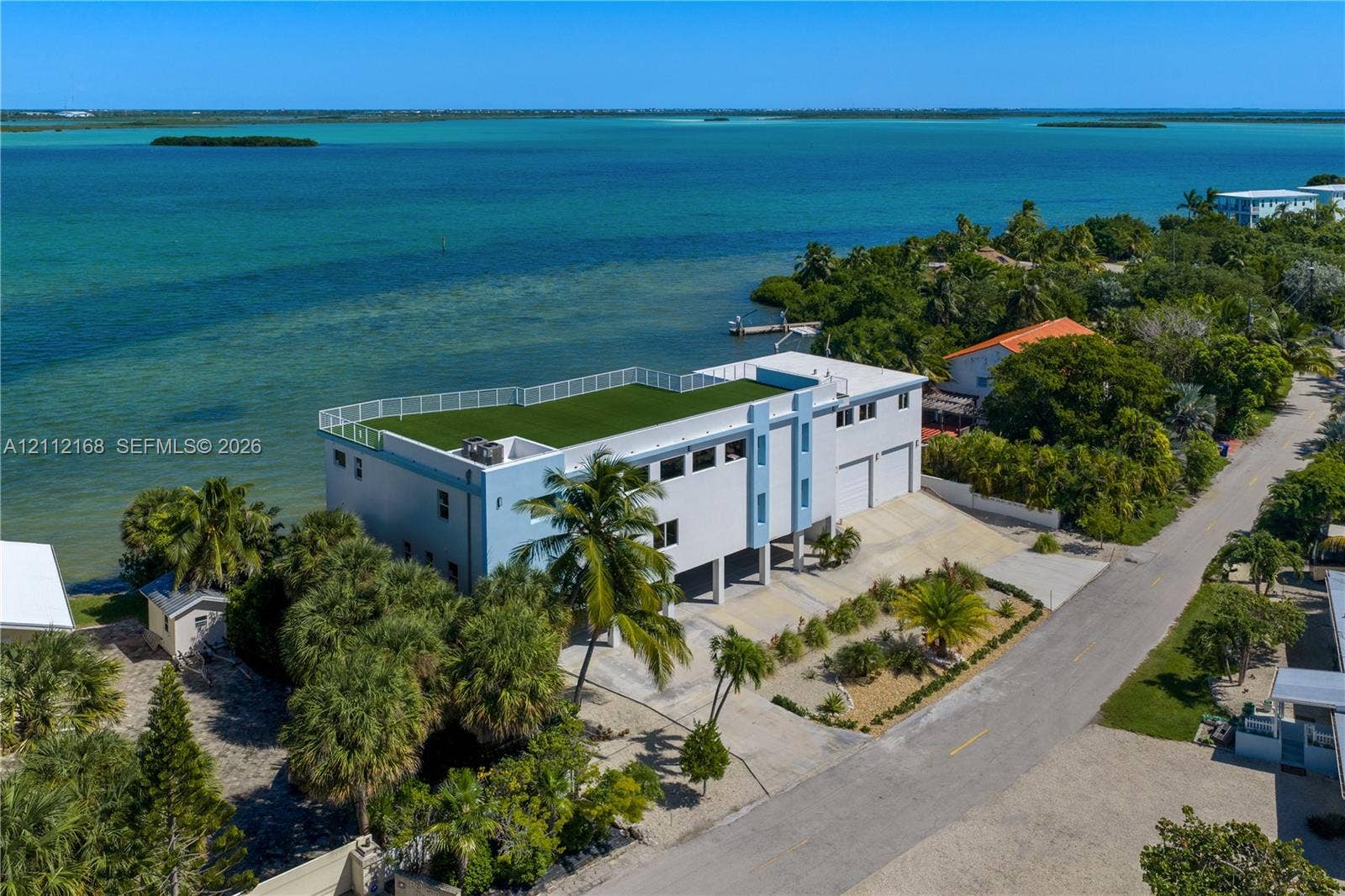 1041 E Buttonwood Drive, Sugarloaf Key, FL 33042 Waterfront multi-story residence featuring a rooftop terrace with synthetic turf, perimeter railing, paved driveway, and attached two-car garage