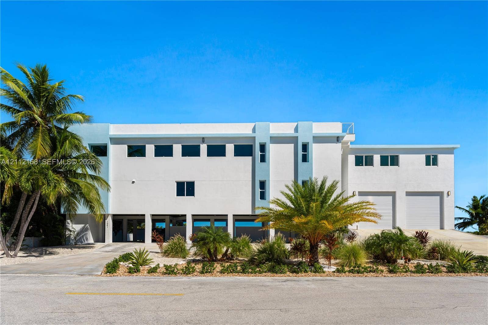 1041 E Buttonwood Drive, Sugarloaf Key, FL 33042 Contemporary multi-level exterior featuring white stucco finish, dual garage bays, expansive windows, and integrated ground-level parking