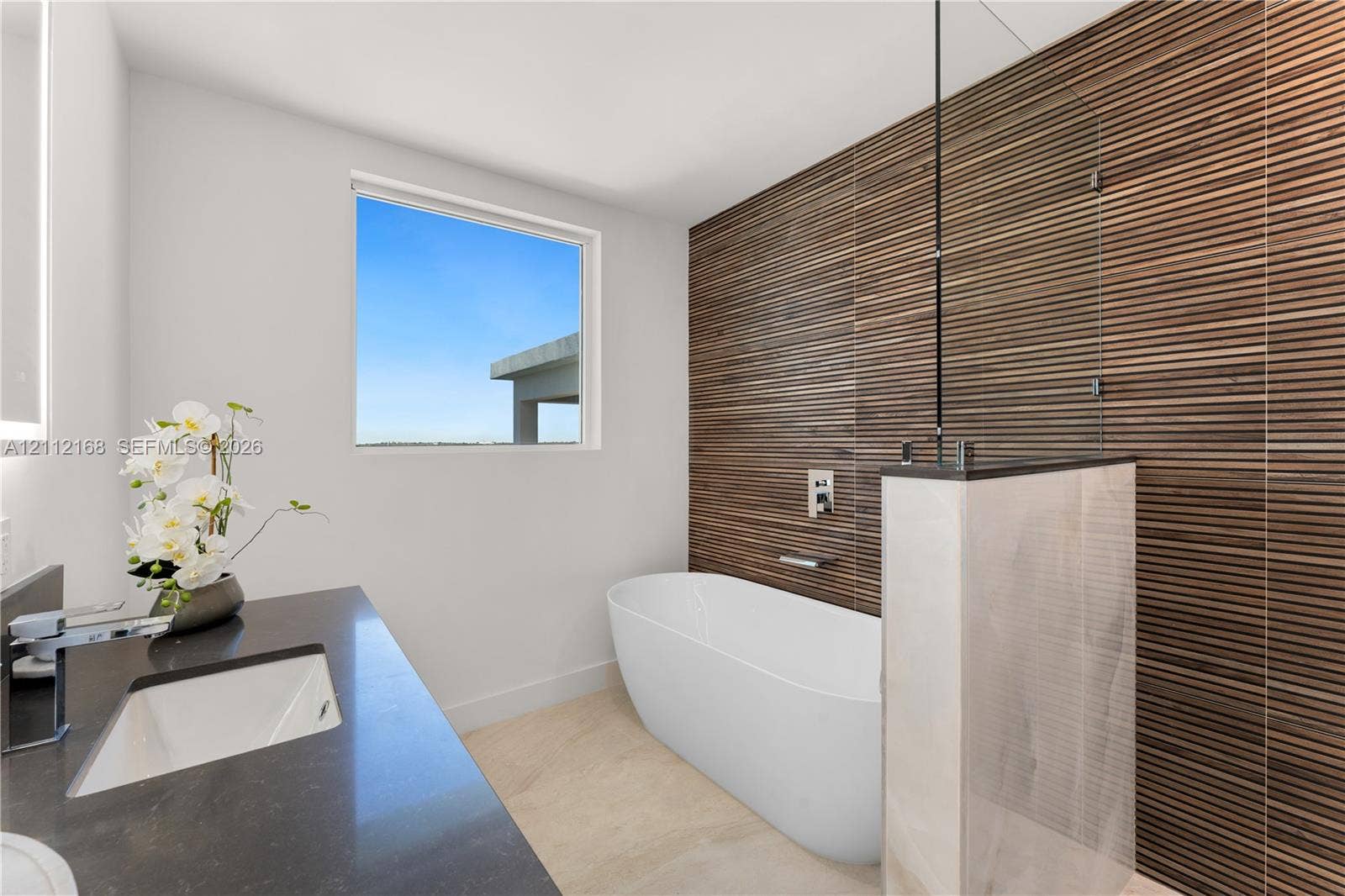 1041 E Buttonwood Drive, Sugarloaf Key, FL 33042 Freestanding soaking tub featuring a wall-mounted faucet, horizontal slatted wood-texture accent wall, glass partition, stone-finish vanity countertop, and rectangular undermount sink