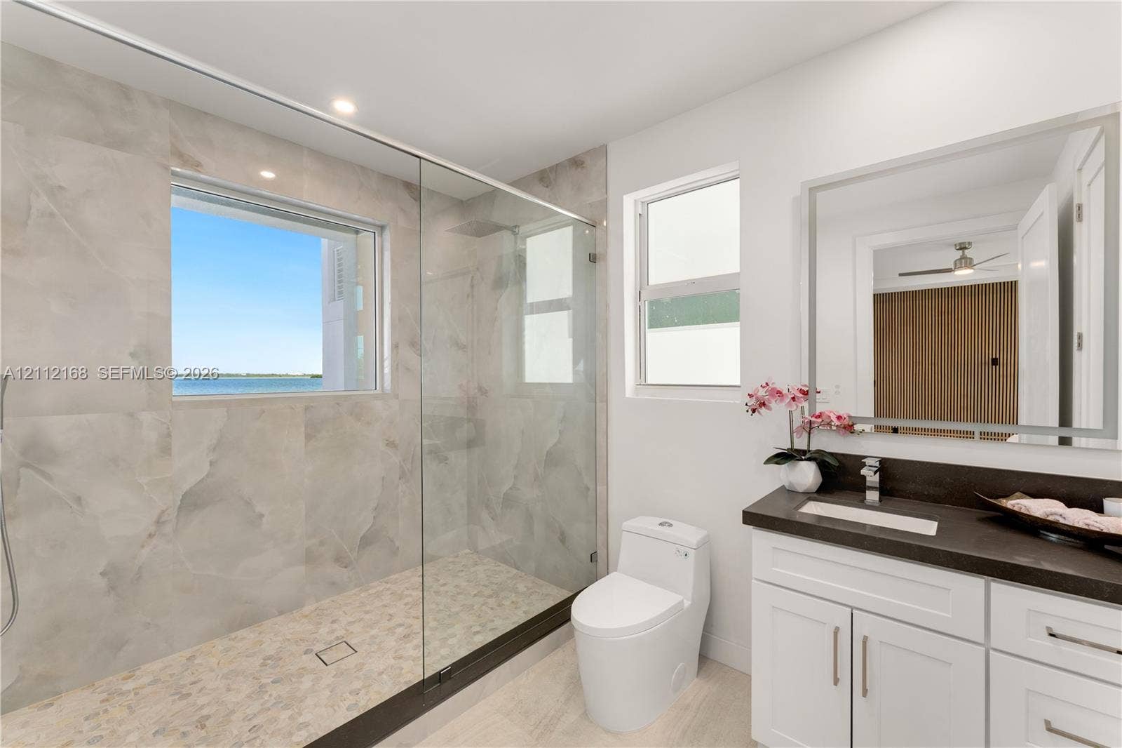 1041 E Buttonwood Drive, Sugarloaf Key, FL 33042 Bathroom featuring a walk-in shower with large-format wall tile and pebble-texture flooring, frameless glass enclosure, dual-pane window, and white cabinetry with a contrasting dark countertop