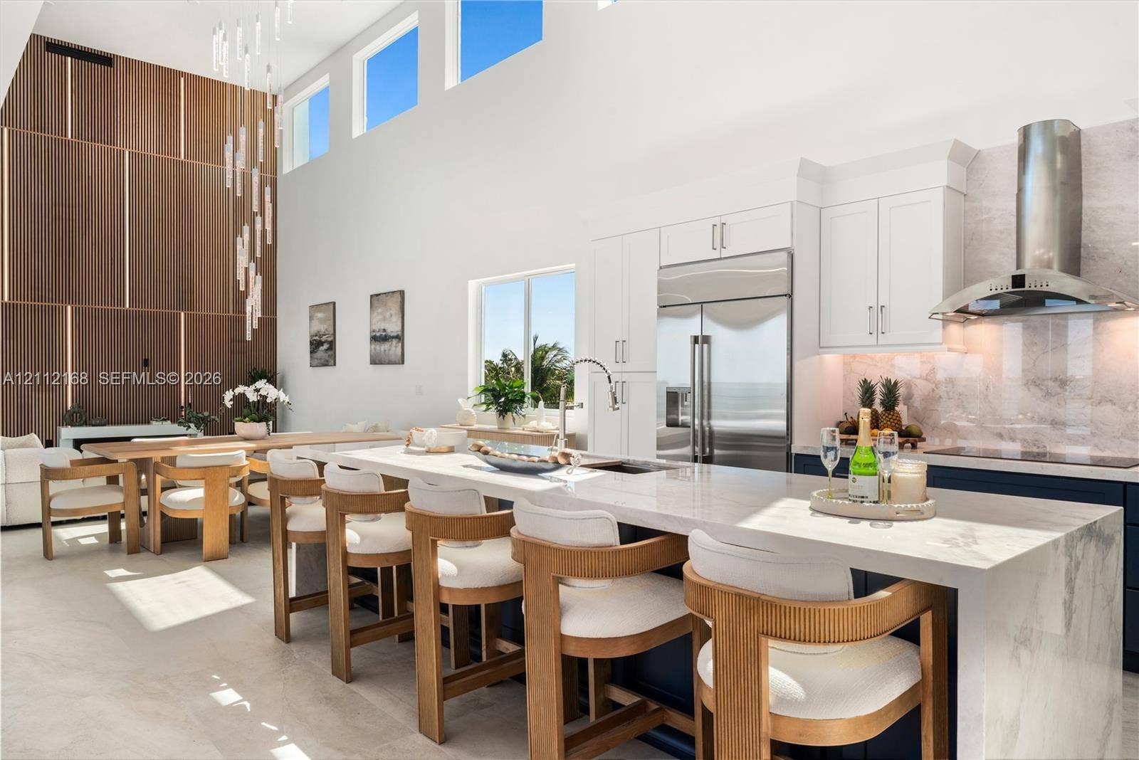 1041 E Buttonwood Drive, Sugarloaf Key, FL 33042 Kitchen featuring a waterfall island with stone countertop, cabinetry with integrated appliances, vertical wood-paneling wall feature, soaring ceilings with transom windows, and a multi-pendant light fixture