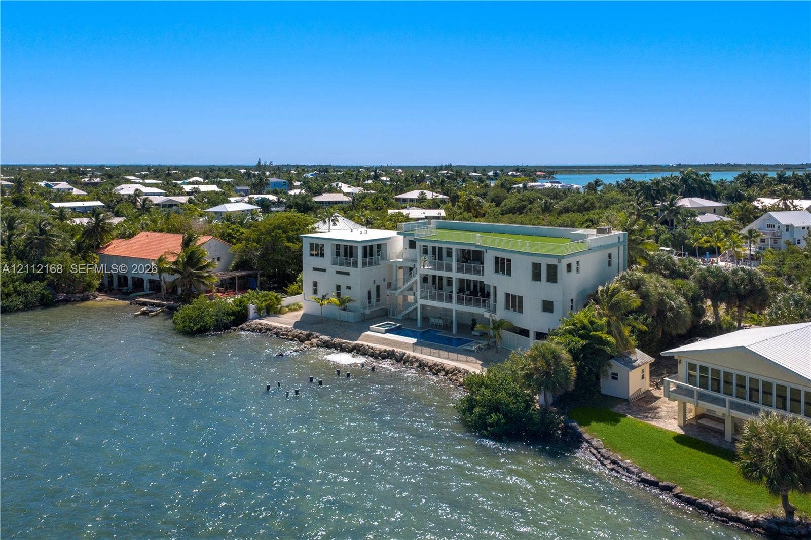 1041 E Buttonwood Drive, Sugarloaf Key, FL 33042 Waterfront multi-story residence featuring a private pool, multiple tiered balconies, a rooftop terrace, and stone shoreline stabilization