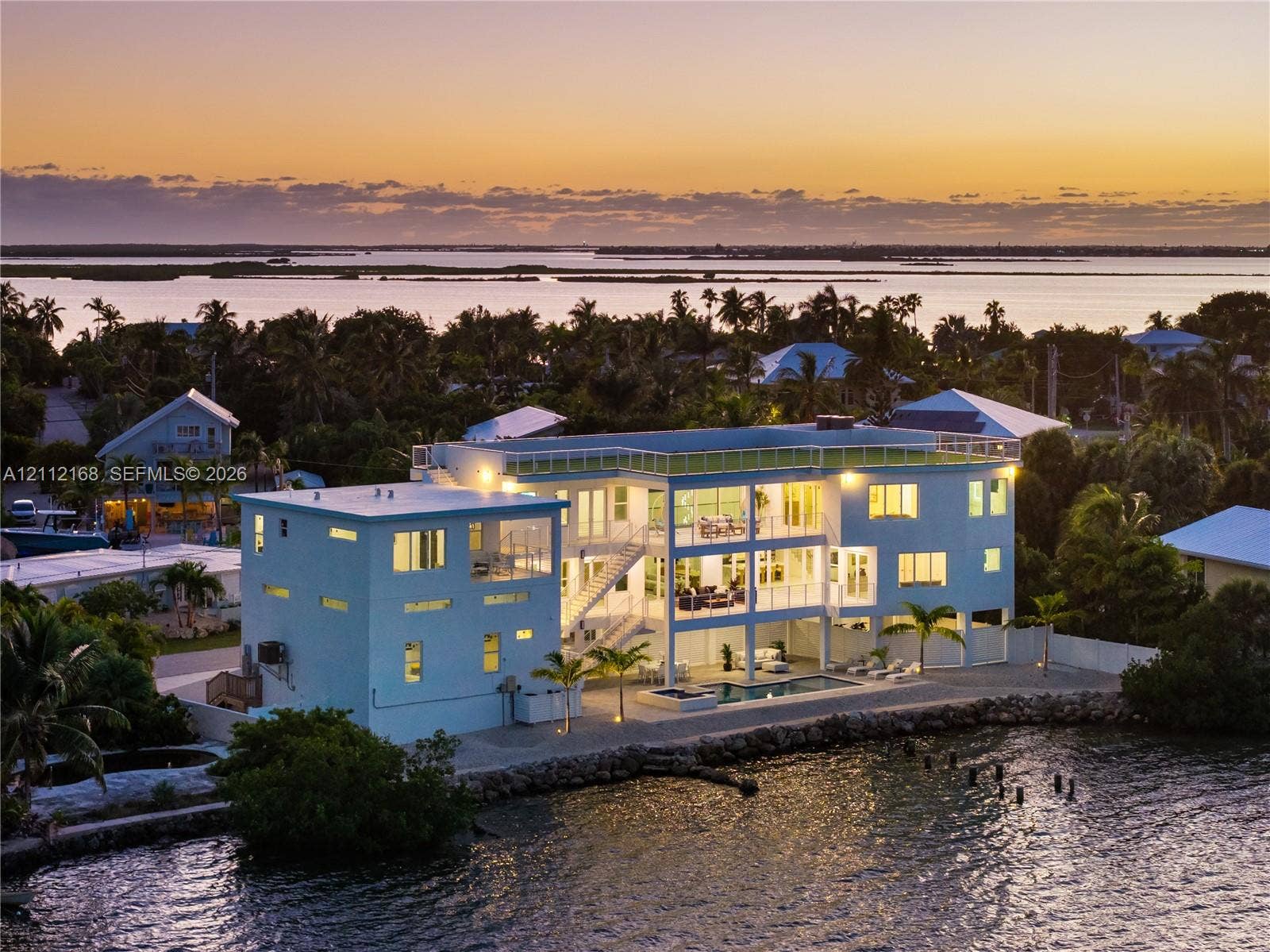 1041 E Buttonwood Drive, Sugarloaf Key, FL 33042 Multi-level waterfront residence featuring a rooftop deck, exterior staircase, ground-level pool, and stone-reinforced shoreline