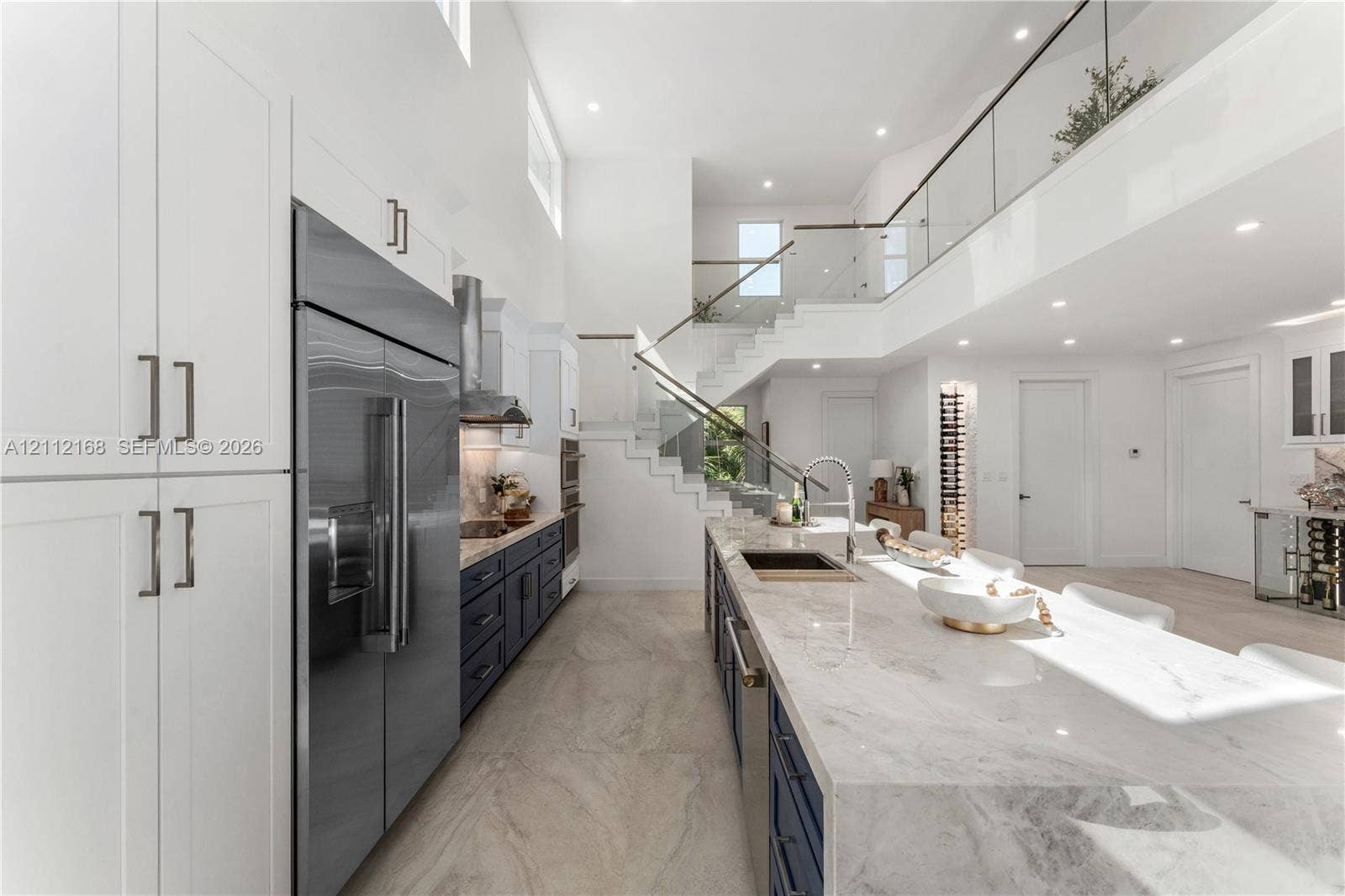 1041 E Buttonwood Drive, Sugarloaf Key, FL 33042 High-ceilinged kitchen featuring dual-tone cabinetry, a waterfall-edge stone island, recessed lighting, and a glass-panel staircase railing