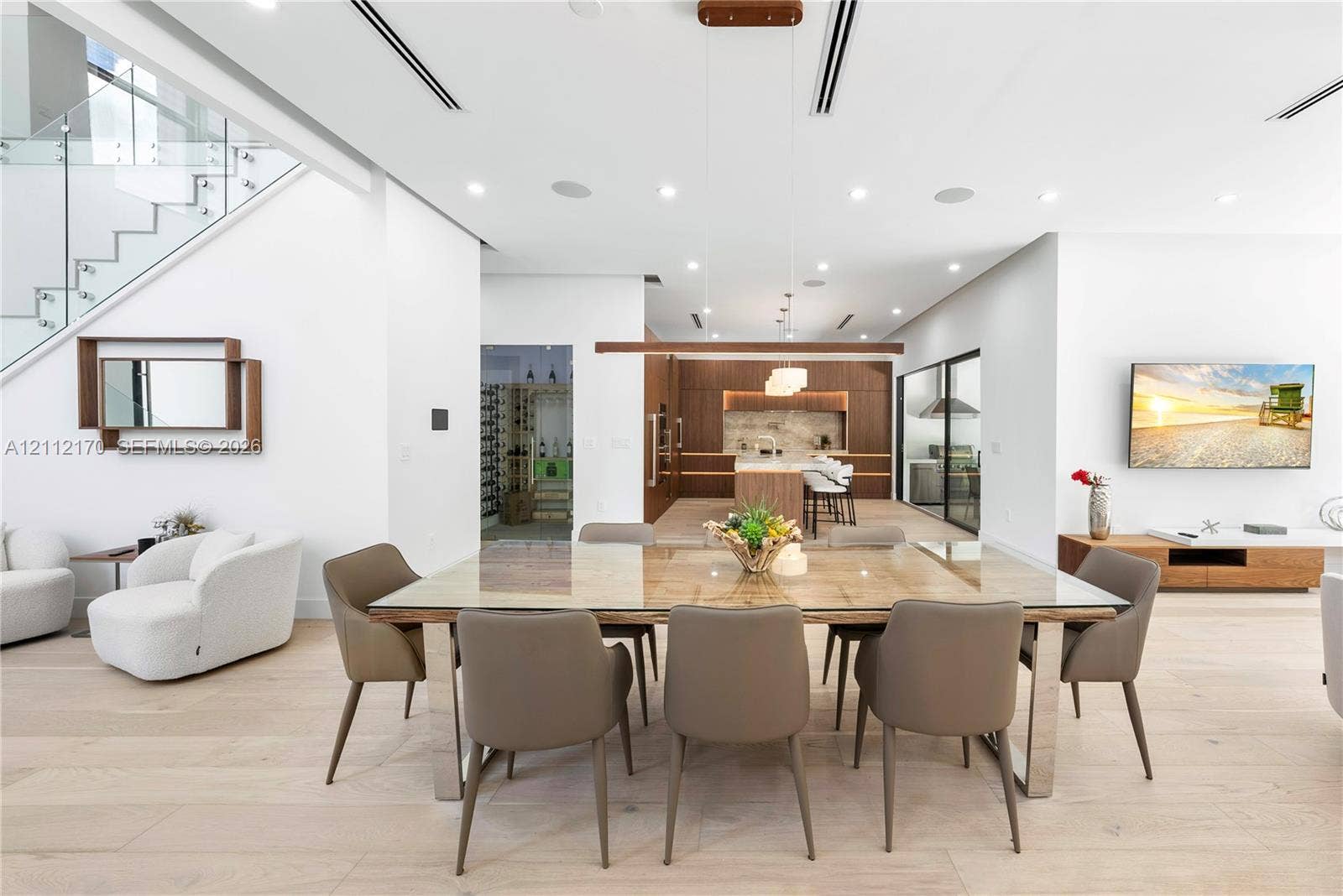 Open-concept interior featuring light wood-finish flooring, glass-railing staircase, linear recessed lighting, built-in temperature-controlled wine storage, and custom cabinetry
