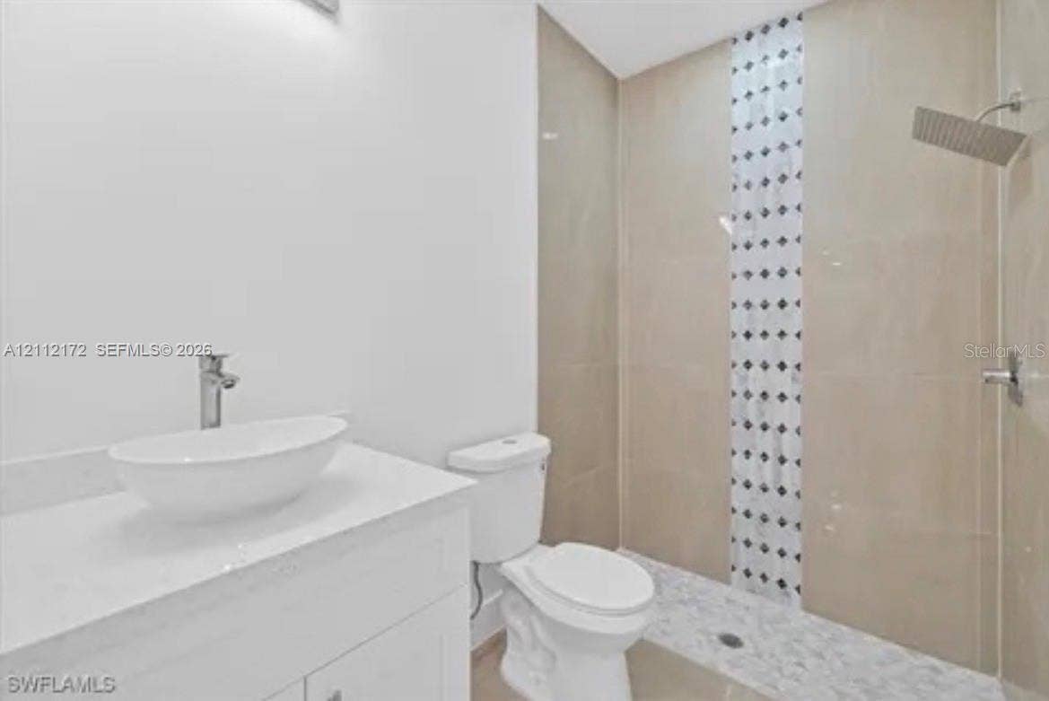 Bathroom featuring a white vanity with a rectangular vessel sink, polished countertop, glass-enclosed shower with decorative vertical tile inlay, and wall-mounted rainfall shower head