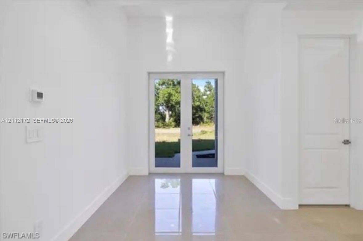 Interior space featuring high ceilings, polished tile flooring, double-panel glass entry doors, and a solid-core interior door
