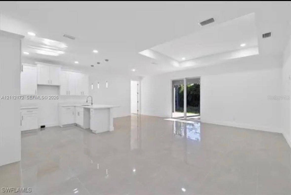 Open-concept floor plan featuring recessed lighting, a coffered ceiling, polished tile flooring, and a kitchen with white cabinetry and a center island