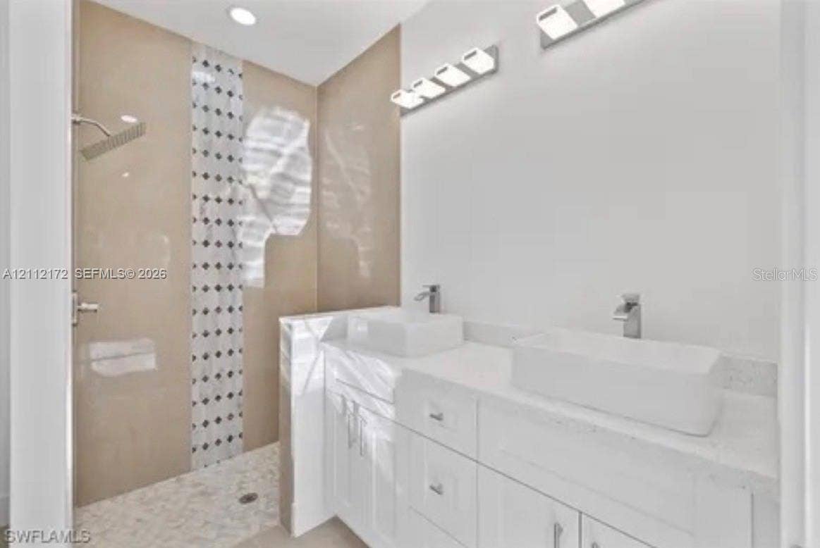Dual white vessel sinks with chrome faucets, stone-topped vanity cabinetry, and a walk-in shower featuring neutral-toned tile work with a vertical mosaic accent