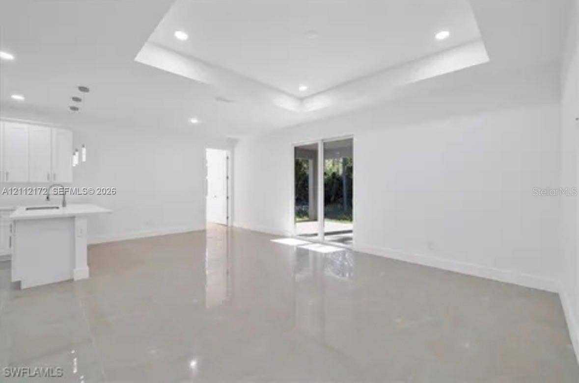 Open-concept interior featuring a tray ceiling, recessed lighting, polished large-format tile flooring, a kitchen island with stone-surface countertop, and sliding glass doors