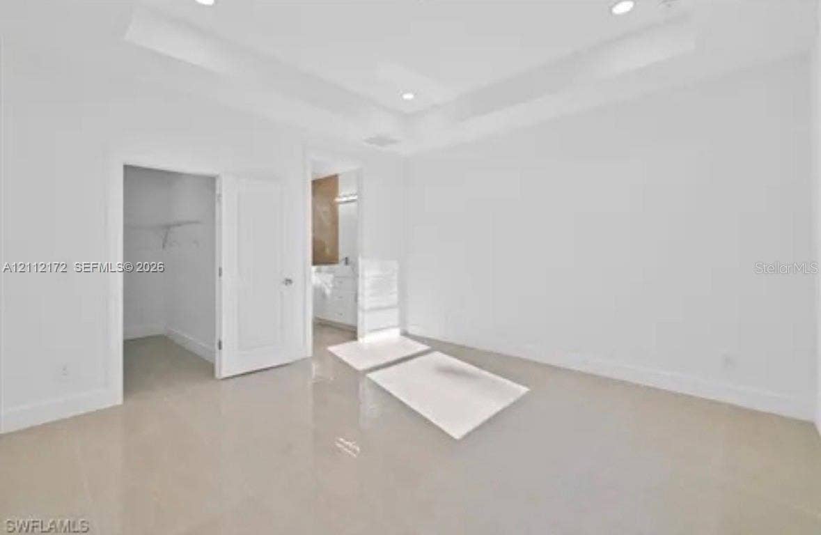 Tray ceiling with recessed lighting, large-format tile flooring, and walk-in closet featuring built-in wire shelving
