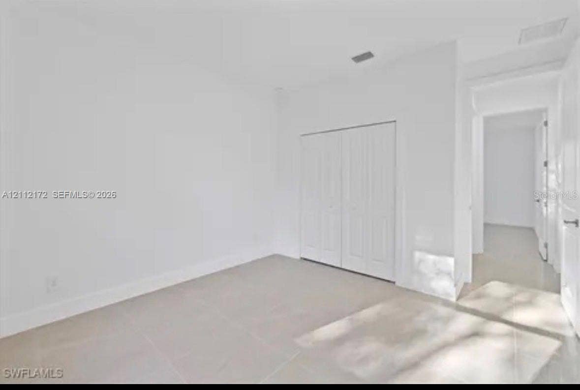 Neutral interior space featuring polished tile flooring, smooth white walls, and a built-in closet with dual paneled doors