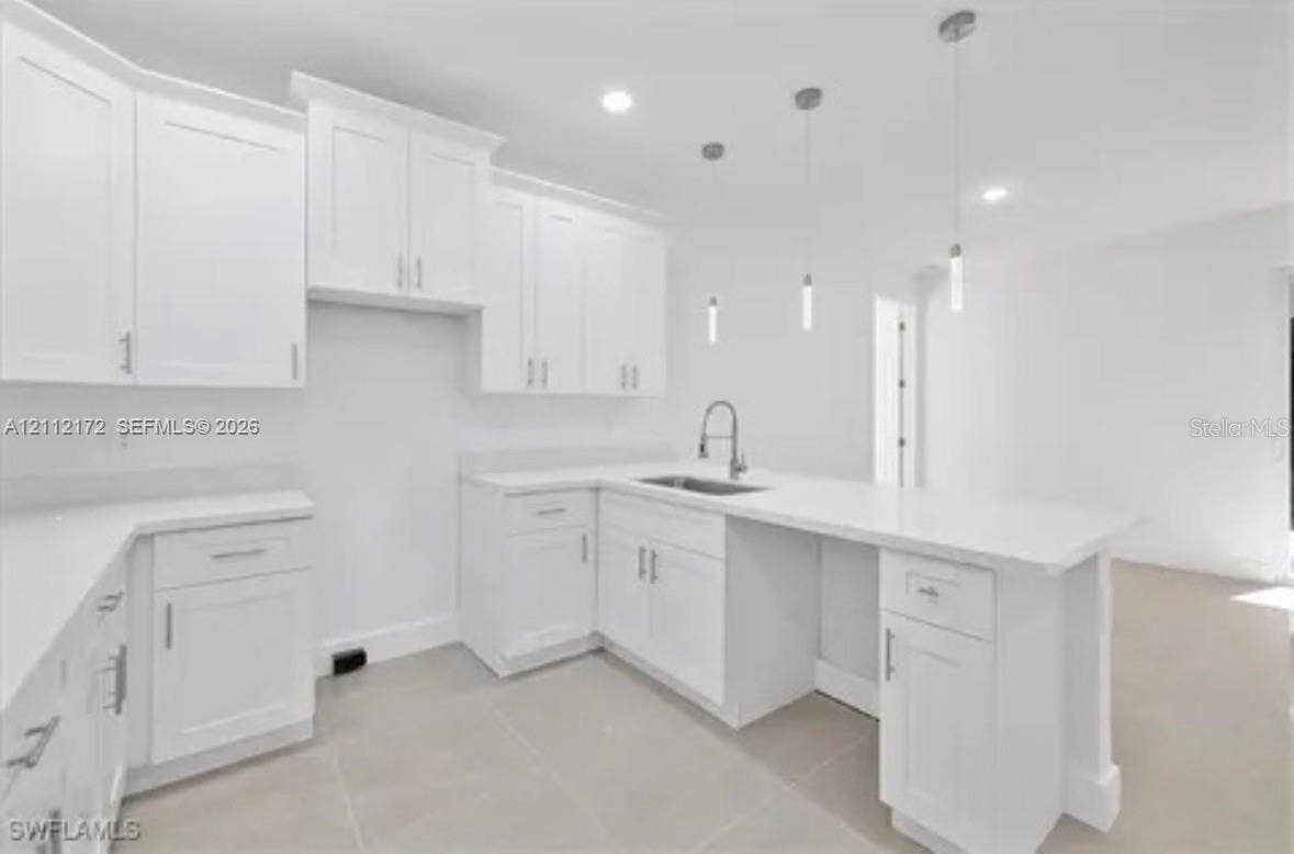 Kitchen featuring white shaker-style cabinetry, solid-surface countertops, a stainless steel undermount sink with a gooseneck faucet, three pendant lights, and light-toned tile flooring