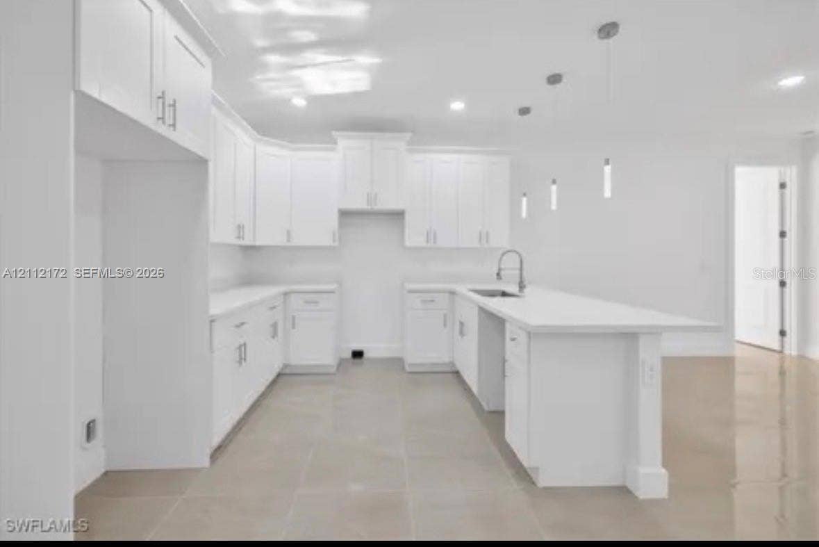 Kitchen featuring white cabinetry, an expansive center island, quartz countertops, a stainless steel undermount sink with a gooseneck faucet, and recessed and pendant lighting