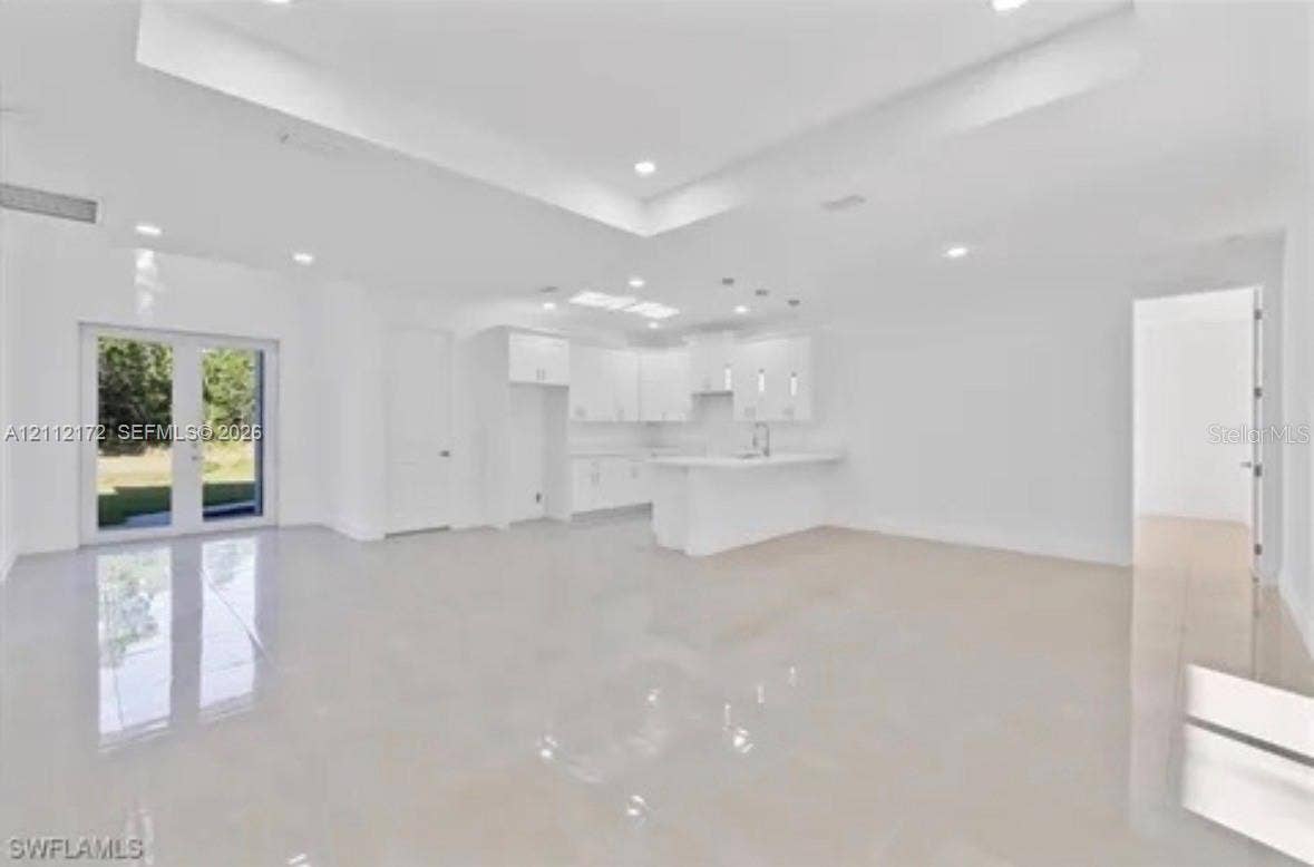 Open-concept living space featuring high tray ceilings, recessed lighting, polished tile flooring, white cabinetry, and double French doors