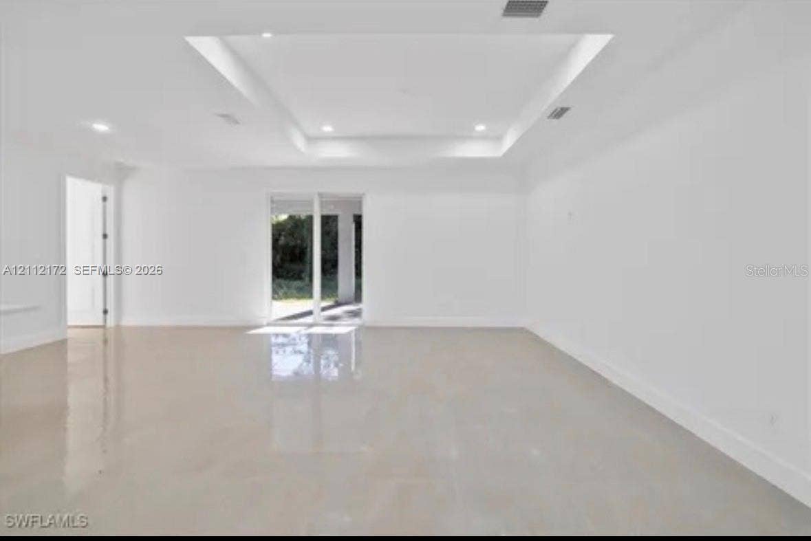 Spacious interior featuring a recessed tray ceiling, polished tile flooring, recessed lighting, and multi-panel sliding glass doors