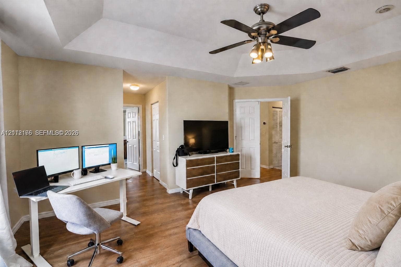 19143 Crystal Street, Weston, FL 33332 Tray ceiling featuring a central multi-blade ceiling fan with integrated lighting, wood-finish flooring, and multiple sets of interior paneled doors