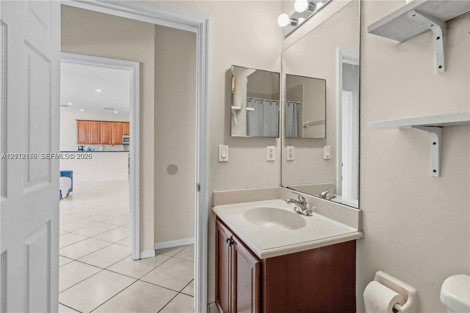19143 Crystal Street, Weston, FL 33332 Bathroom featuring a dark wood-finish vanity, integrated sink, large wall-mounted mirror, and wall-mounted shelving