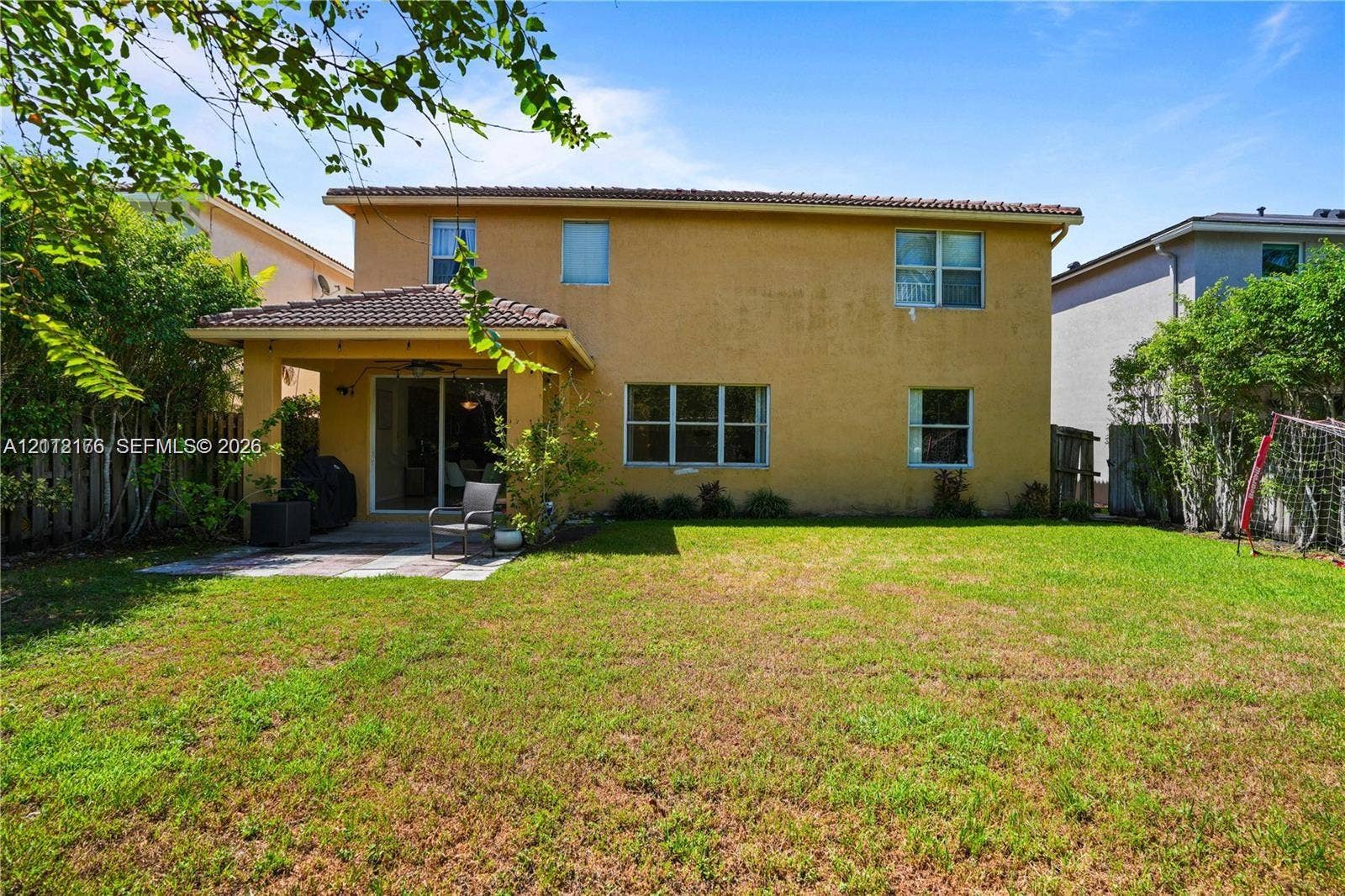 19143 Crystal Street, Weston, FL 33332 Rear exterior featuring a two-story stucco facade, a covered concrete patio, a tiled roof, and a fenced-in grassy yard