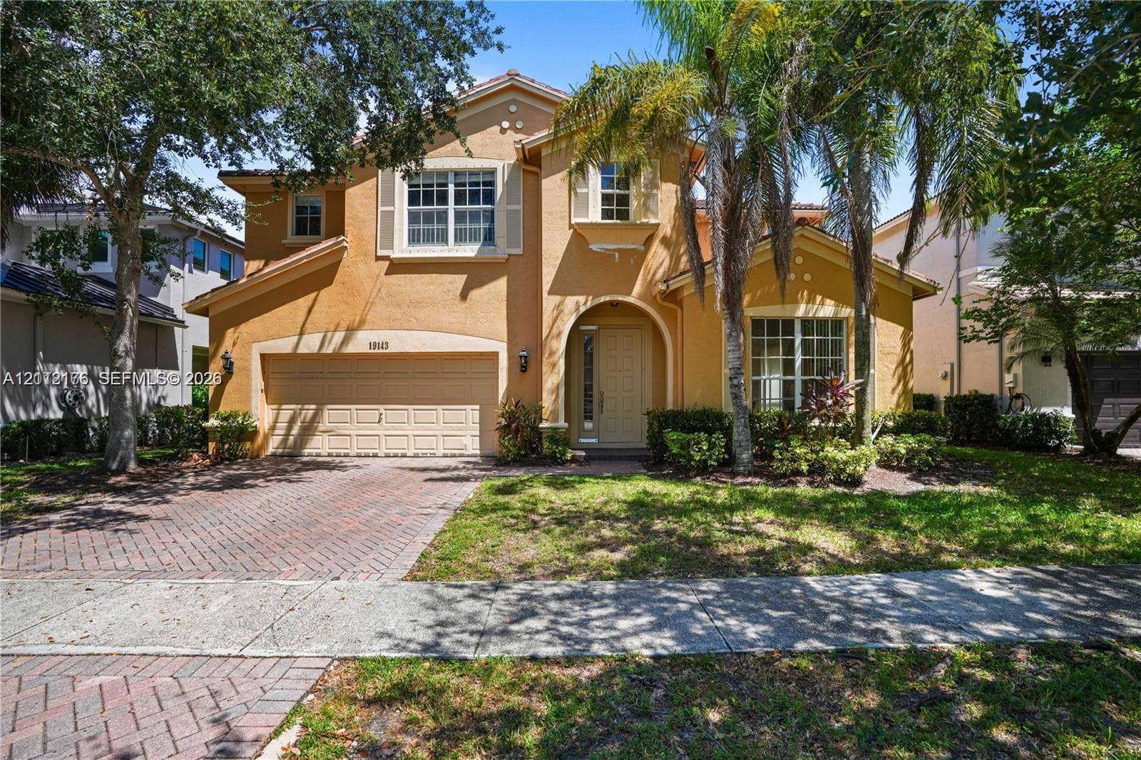 19143 Crystal Street, Weston, FL 33332 Two-story stucco exterior featuring a tiled roof, arched entryway, brick-patterned paved driveway, and decorative window shutters