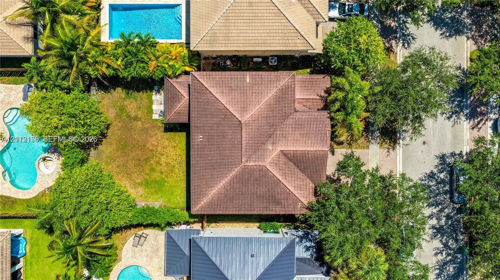 19143 Crystal Street, Weston, FL 33332 Aerial perspective featuring a hip roof structure, paved driveway, landscaped grounds with mature trees, and a swimming pool
