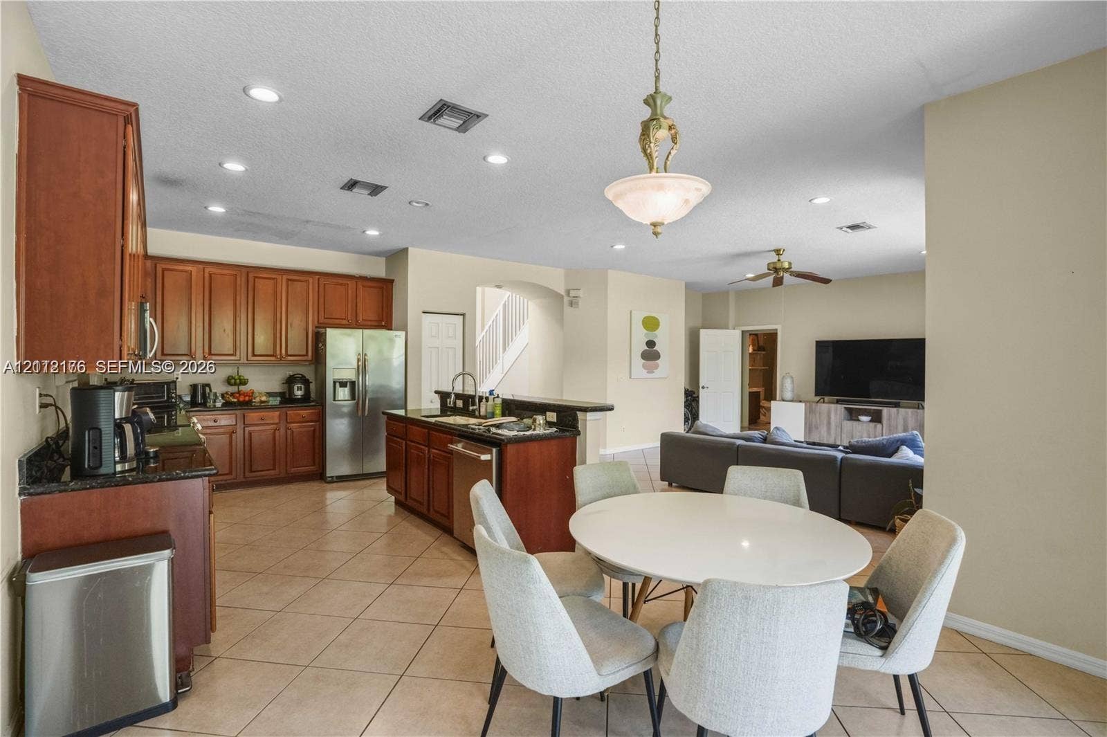 19143 Crystal Street, Weston, FL 33332 Kitchen featuring medium-tone wood cabinetry, granite countertops, a center island with integrated sink, stainless steel appliances, and tiled flooring
