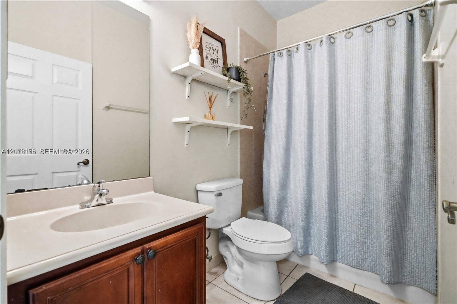 19143 Crystal Street, Weston, FL 33332 Bathroom featuring a wood-finish vanity with an integrated oval sink, full-width wall mirror, tile flooring, and wall-mounted shelving