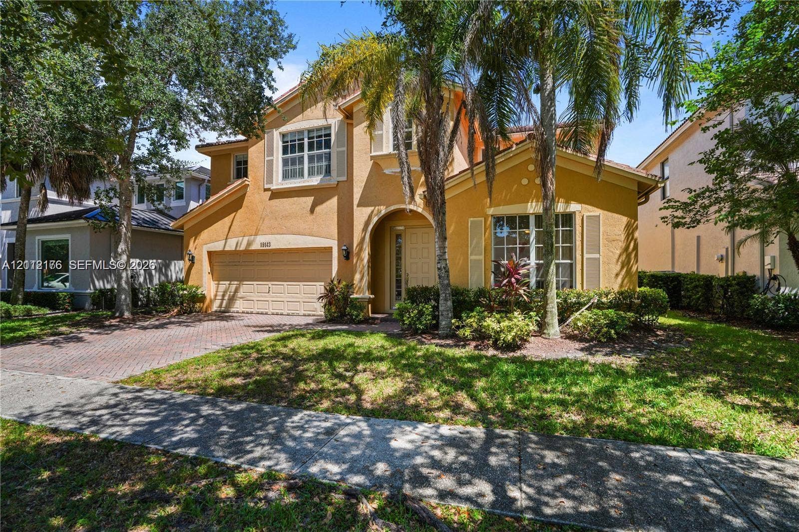 19143 Crystal Street, Weston, FL 33332 Stucco exterior featuring an arched entryway, shuttered windows, a two-car garage, and a brick-paver driveway