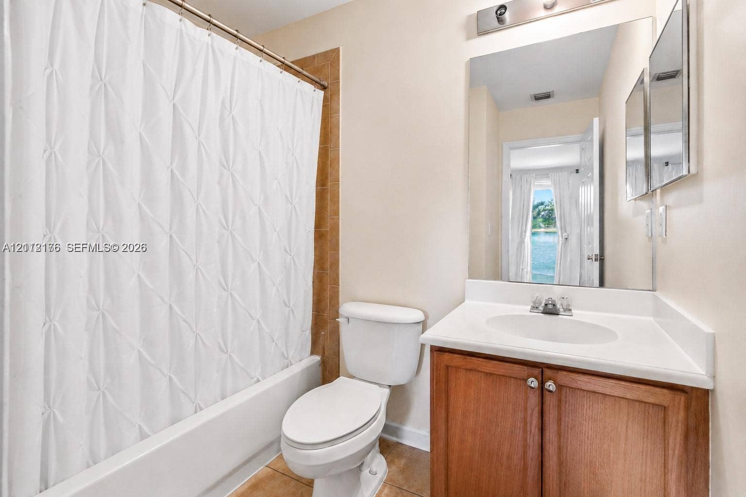 19143 Crystal Street, Weston, FL 33332 Bathroom featuring a wood-finish vanity with a solid-surface countertop, integrated basin, large wall-mounted mirror, and a tile-surround bathtub
