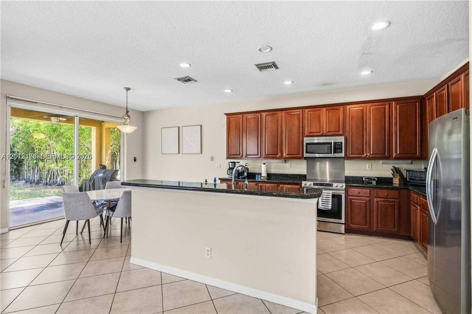 19143 Crystal Street, Weston, FL 33332 Kitchen featuring dark wood cabinetry, a breakfast bar with stone-finish countertops, stainless steel appliances, recessed lighting, and tile flooring