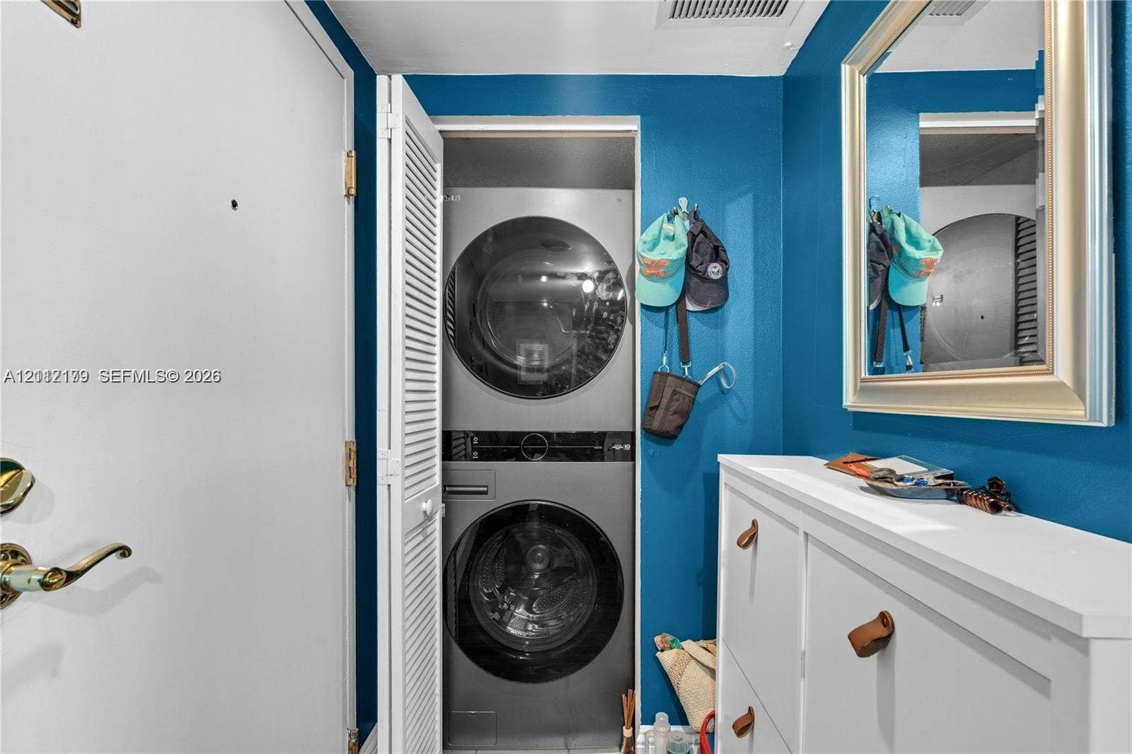 800 Claughton Island Drive, #1604, Miami, Miami, FL 33131 Stackable stainless steel washer and dryer unit, wall-mounted mirror with a metallic frame, and white louvered closet doors
