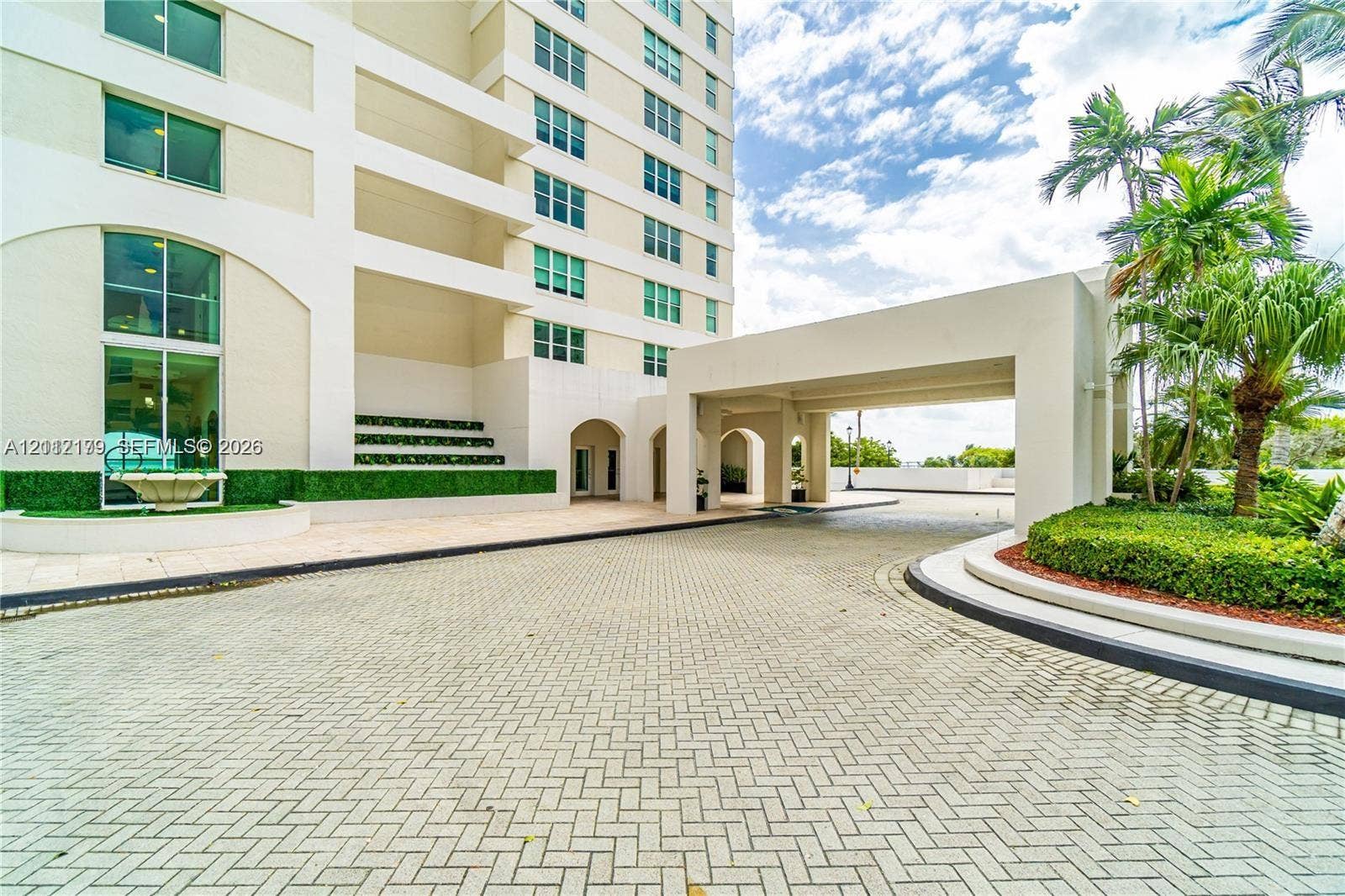 800 Claughton Island Drive, #1604, Miami, Miami, FL 33131 Covered porte-cochre entry featuring paver hardscaping, multi-story facade with expansive glass windows, and manicured landscaping