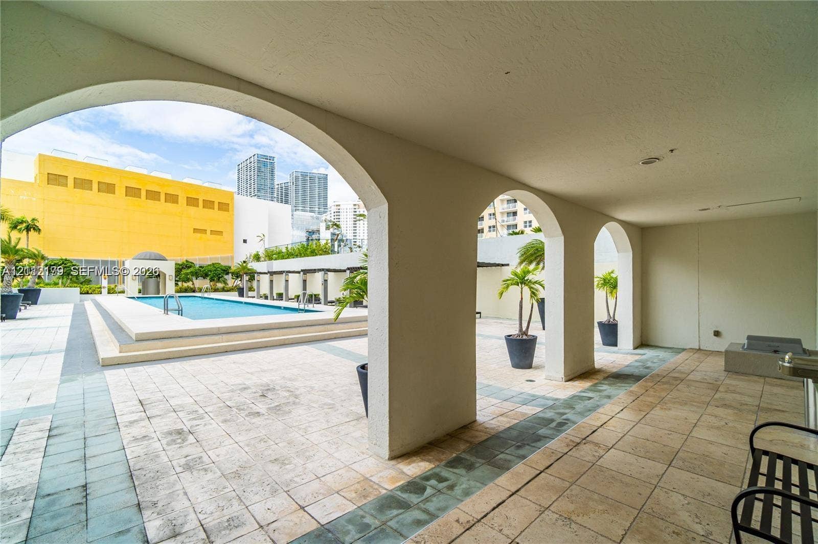 800 Claughton Island Drive, #1604, Miami, Miami, FL 33131 Covered patio featuring arched architectural details and stone-tile flooring, overlooking a swimming pool with tiered concrete decking