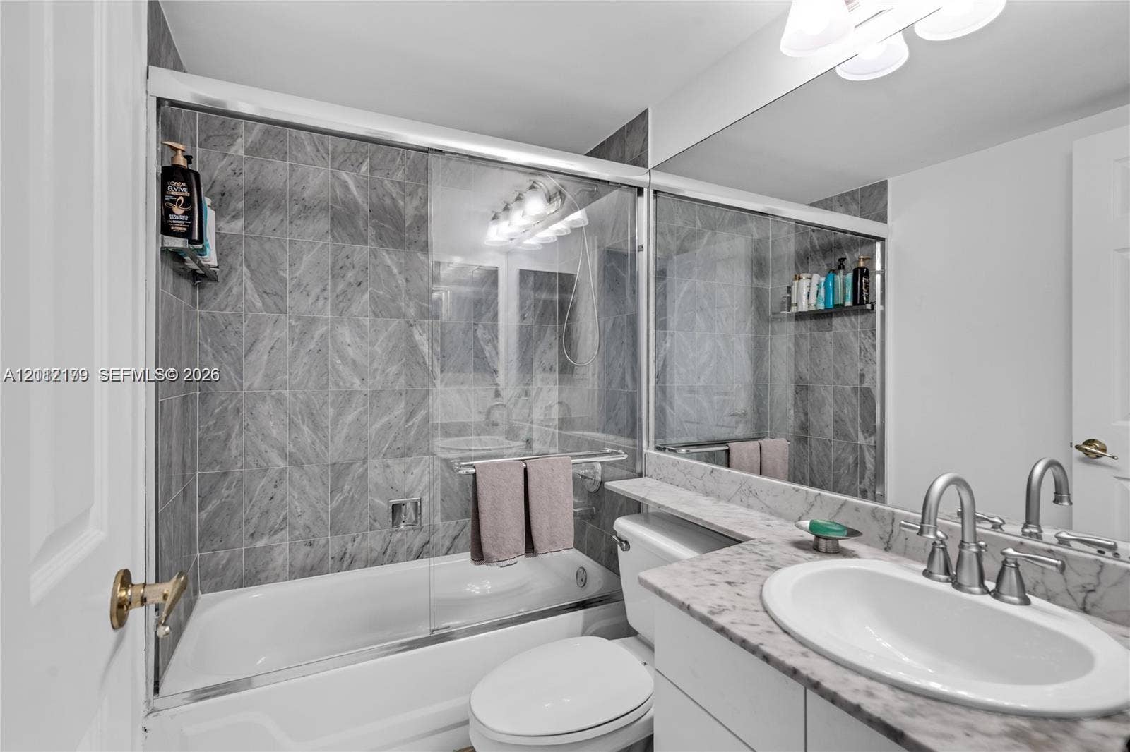 800 Claughton Island Drive, #1604, Miami, Miami, FL 33131 Bathroom featuring a shower-tub combination with glass enclosure, full-height stone-finish wall tile, a stone-top vanity with integrated sink, and an expansive wall-to-wall vanity mirror