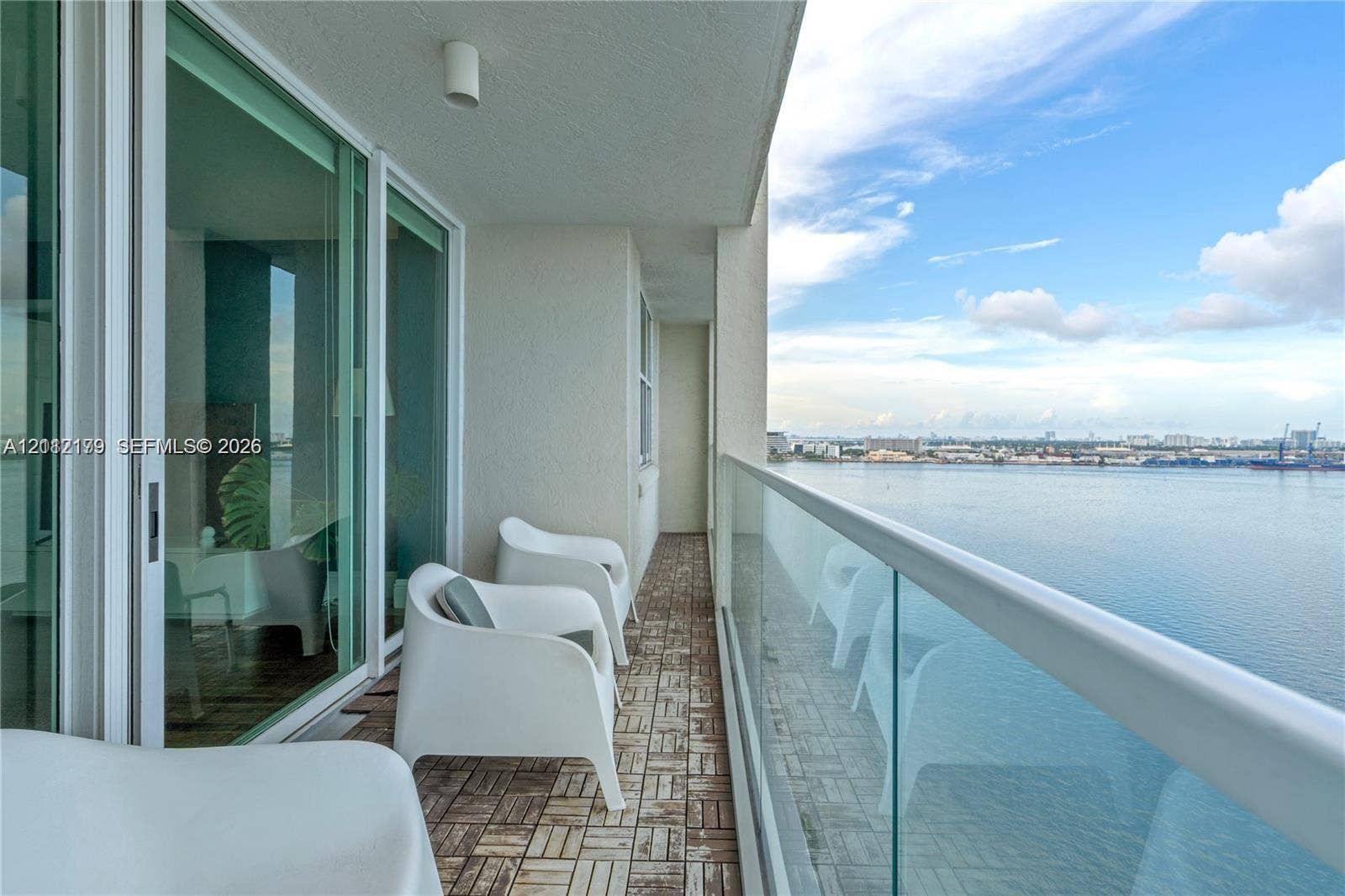 800 Claughton Island Drive, #1604, Miami, Miami, FL 33131 Covered balcony featuring wood-finish deck tiling, glass panel railing, floor-to-ceiling sliding glass doors, and direct water frontage
