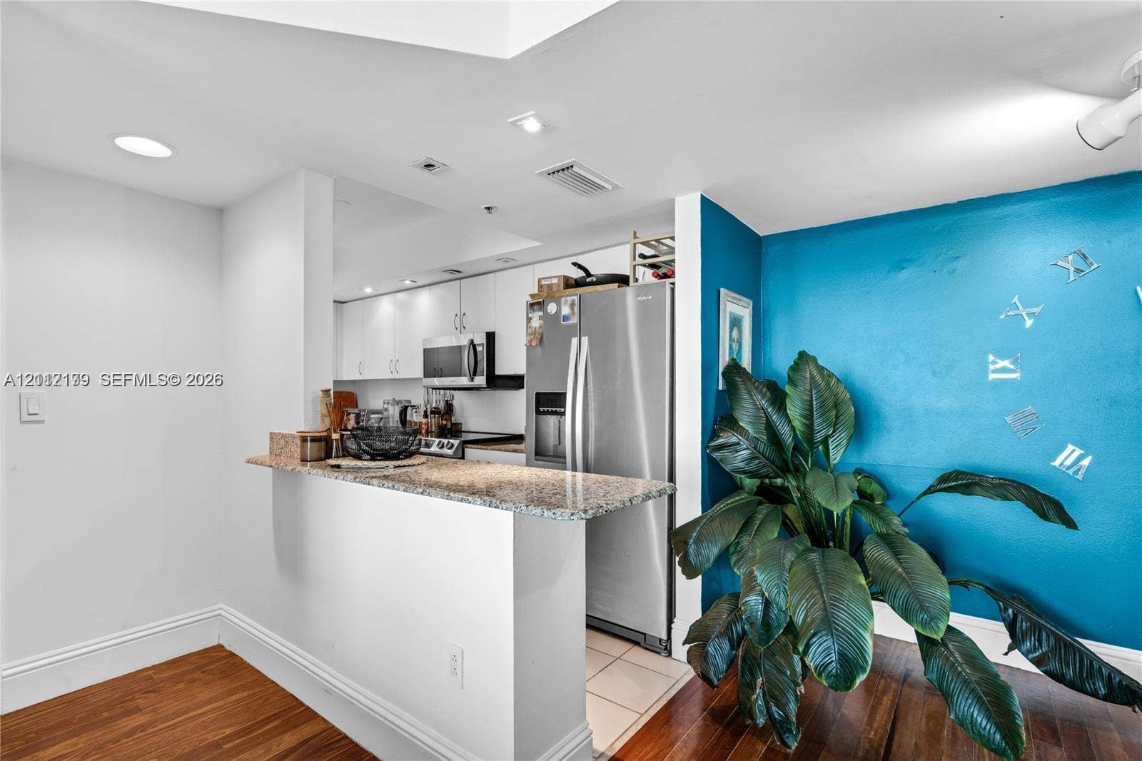 800 Claughton Island Drive, #1604, Miami, Miami, FL 33131 Kitchen featuring white cabinetry, stone-surface breakfast bar, stainless steel refrigerator, built-in microwave, and wood-finish flooring